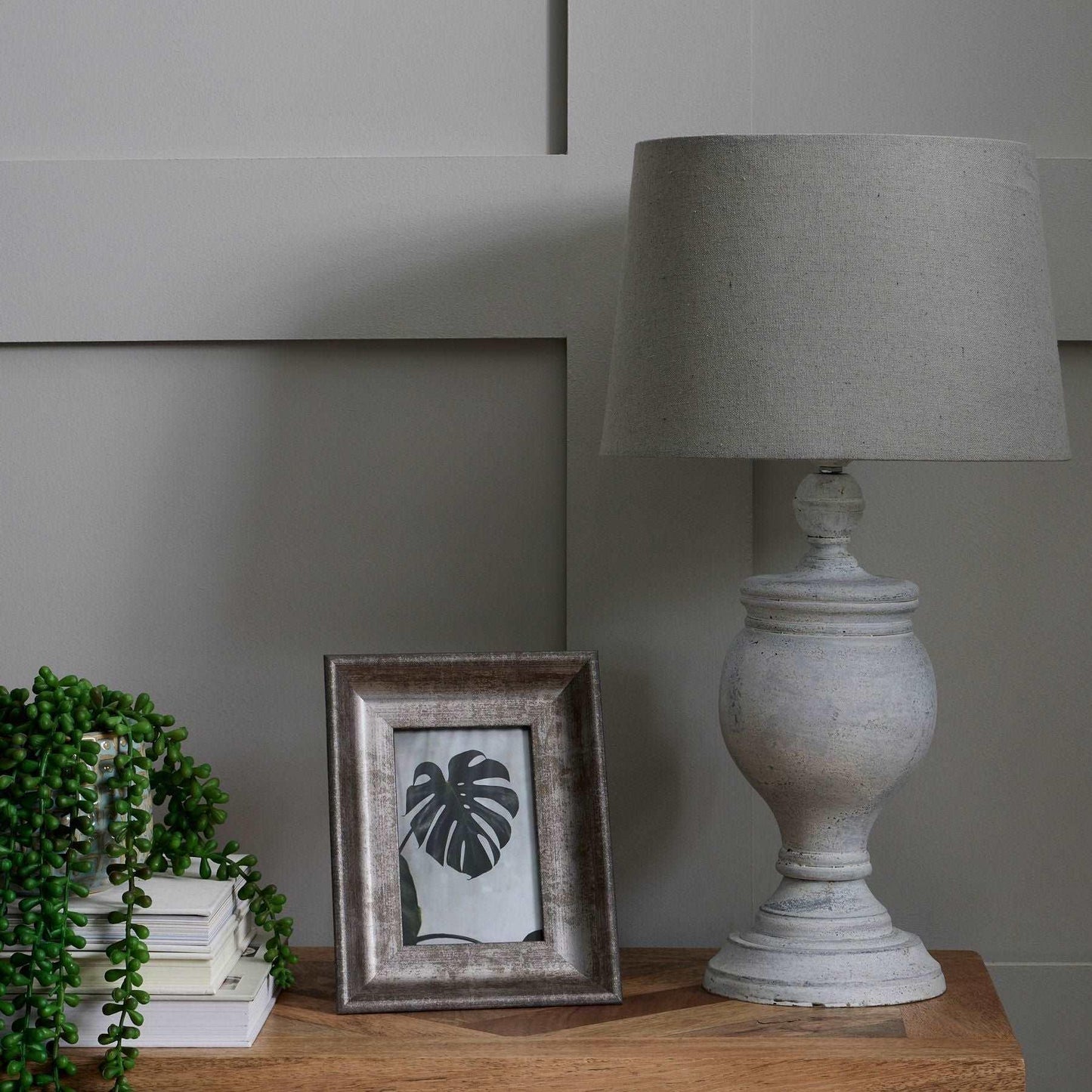 Elegant neutral table with grey lamp, houseplant, books, and framed botanical art