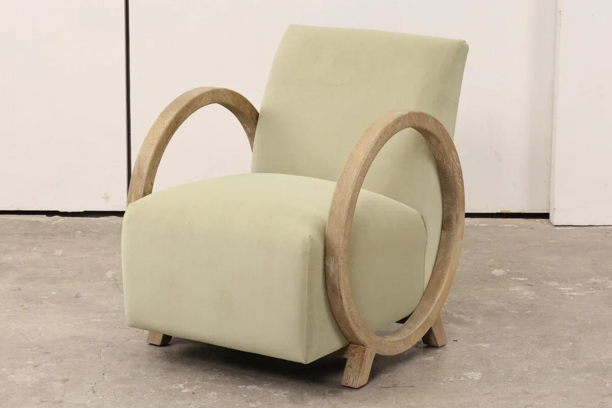 Sage green accent chair with circular wooden arms and plush upholstery on concrete floor