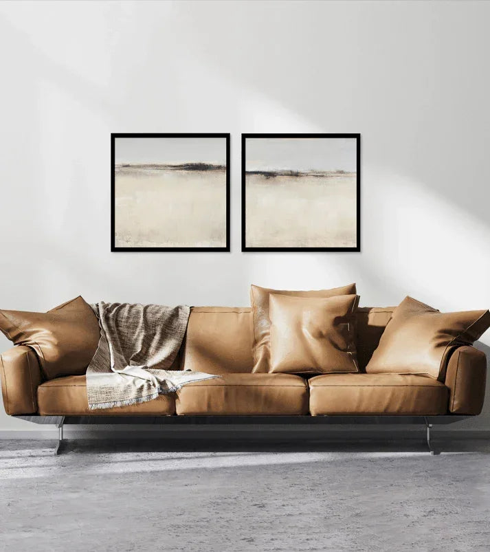 Modern tan leather sofa with neutral throw blanket and pillows, two abstract wall art pieces above.