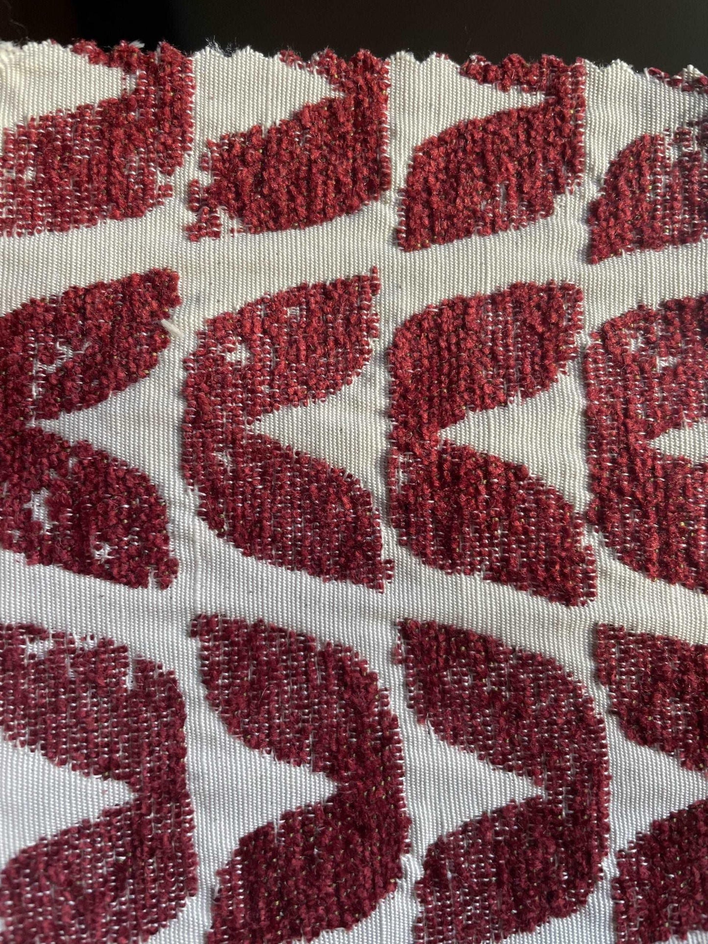 Close-up of red patterned upholstery fabric with geometric leaf motifs on a cream background