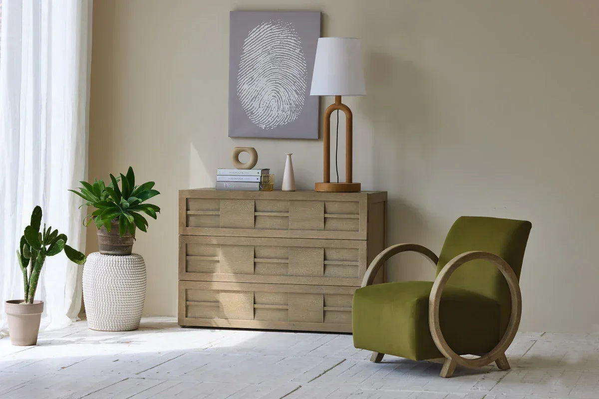 Modern living room with green armchair, wooden dresser, indoor plants, and minimalist decor