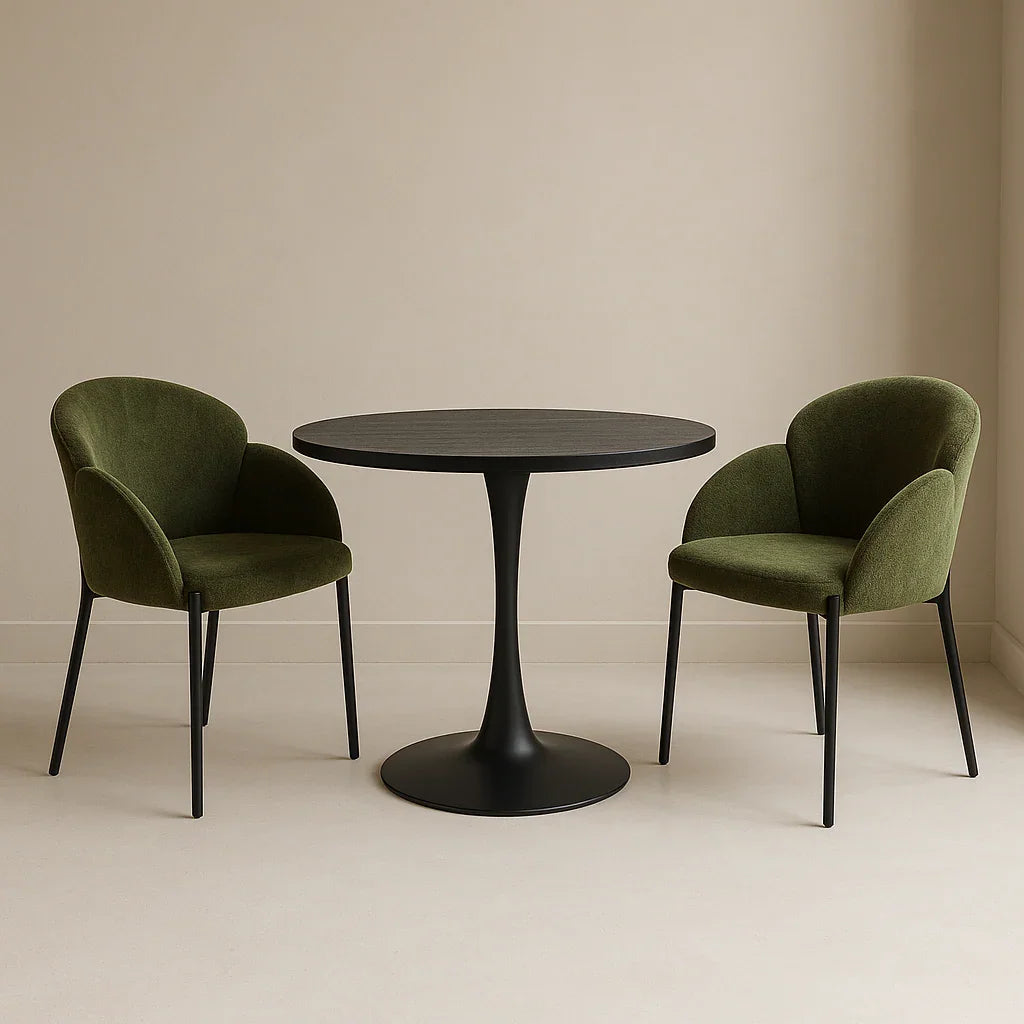 Modern round black pedestal dining table with two green velvet chairs in a minimal room